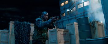 Movie still from “Expend4bles” (2023), directed by Scott Waugh – A man holding a gun while standing next to a building; Medium shot, Over the shoulder angle