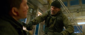 Movie still from “Expend4bles” (2023), directed by Scott Waugh – A man in a hat and jacket is fighting with another man; Medium shot, Over the shoulder angle