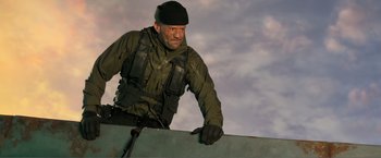 Movie still from “Expend4bles” (2023), directed by Scott Waugh – A man in a black hat is holding a snowboard; Medium shot, Low angle