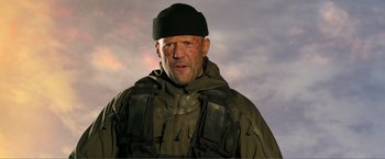 Movie still from “Expend4bles” (2023), directed by Scott Waugh – A man in a black hat and a green jacket; Close Up shot, Low angle