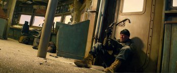 Movie still from “Expend4bles” (2023), directed by Scott Waugh – A man sitting on the ground holding a gun; Wide shot, Low angle