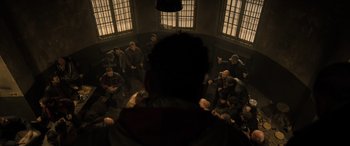 Movie still from “Extraction II” (2023), directed by Sam Hargrave – A group of people sitting in a room with windows; Wide shot, High angle