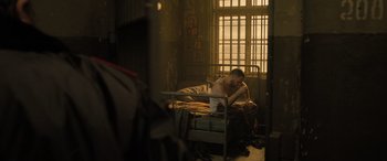 Movie still from “Extraction II” (2023), directed by Sam Hargrave – A man sitting on top of a bed next to a window; Medium shot, High angle