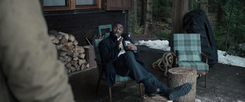 Movie still from “Extraction II” (2023), directed by Sam Hargrave – A man sitting in a chair holding a cell phone; Medium shot, High angle