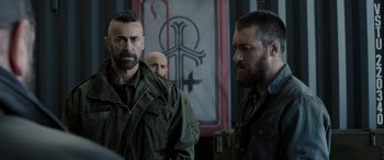 Movie still from “Extraction II” (2023), directed by Sam Hargrave – Two men standing next to each other in front of a painting; Medium shot, Over the shoulder angle