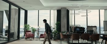 Movie still from “Extraction II” (2023), directed by Sam Hargrave – A young man walking in a room with a large window; Wide shot, Over the shoulder angle