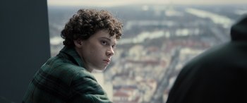 Movie still from “Extraction II” (2023), directed by Sam Hargrave – A young man with curly hair looking out of a window; Close Up shot, Low angle