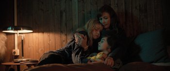 Movie still from “Extraction II” (2023), directed by Sam Hargrave – Two women and a child laying on a bed together; Medium shot, High angle