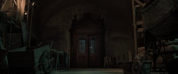 Movie still from “Extraction II” (2023), directed by Sam Hargrave – An empty room with a large wooden door; Wide shot, Low angle