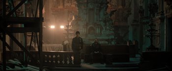 Movie still from “Extraction II” (2023), directed by Sam Hargrave – Two men sitting on benches in front of an ornate building; Wide shot, Low angle
