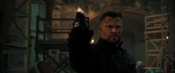 Movie still from “Extraction II” (2023), directed by Sam Hargrave – A man holding a gun while standing next to a building; Close Up shot, Over the shoulder angle