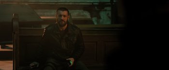 Movie still from “Extraction II” (2023), directed by Sam Hargrave – A man sitting on top of a bench holding a cell phone; Medium shot, High angle