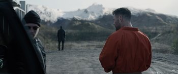 Movie still from “Extraction II” (2023), directed by Sam Hargrave – A man standing in front of another man on a dirt field; Wide shot, Over the shoulder angle