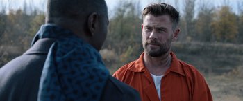 Movie still from “Extraction II” (2023), directed by Sam Hargrave – A man in an orange shirt talking to another man; Close Up shot, Over the shoulder angle