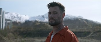 Movie still from “Extraction II” (2023), directed by Sam Hargrave – A person wearing a red shirt near a mountain; Close Up shot, Over the shoulder angle