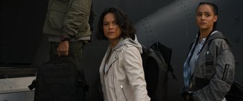 Movie still from “F9: The Fast Saga” (2021), directed by Justin Lin – A woman in a white jacket standing in front of an airplane; Medium shot, Over the shoulder angle