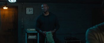 Movie still from “F9: The Fast Saga” (2021), directed by Justin Lin – A man holding a green backpack in a dark room; Medium shot, Over the shoulder angle