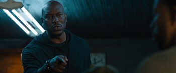 Movie still from “F9: The Fast Saga” (2021), directed by Justin Lin – A man standing in a dark room holding something in his hand; Close Up shot, Over the shoulder angle