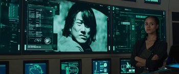 Movie still from “F9: The Fast Saga” (2021), directed by Justin Lin – A large television screen showing a man with long hair; Close Up shot, Over the shoulder angle