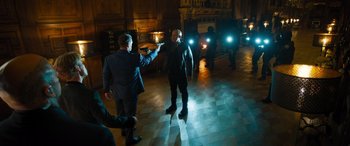 Movie still from “F9: The Fast Saga” (2021), directed by Justin Lin – Two men in suits are standing in a room with lights on; Wide shot, Over the shoulder angle