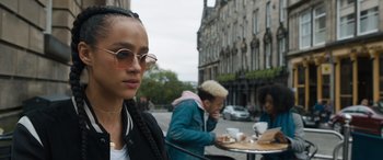 Movie still from “F9: The Fast Saga” (2021), directed by Justin Lin – A woman in a black jacket is sitting at an outdoor table; Close Up shot, Over the shoulder angle