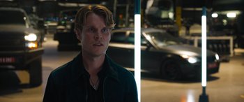 Movie still from “F9: The Fast Saga” (2021), directed by Justin Lin – A man standing next to a pole in a parking lot; Close Up shot, Over the shoulder angle