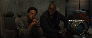 Movie still from “F9: The Fast Saga” (2021), directed by Justin Lin – Two men sitting next to each other in a dark room; Medium shot, Low angle