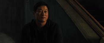 Movie still from “F9: The Fast Saga” (2021), directed by Justin Lin – A man in a black jacket is sitting in a dark room; Close Up shot, Over the shoulder angle