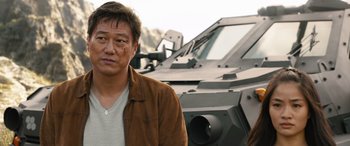 Movie still from “F9: The Fast Saga” (2021), directed by Justin Lin – A man standing in front of an armored vehicle; Medium shot, Low angle