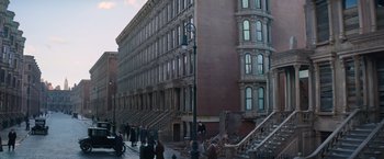 Movie still from “Fantastic Beasts and Where to Find Them” (2016), directed by David Yates – People are walking down the sidewalk in front of a building; Extreme Wide shot, High angle