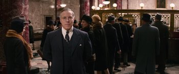 Movie still from “Fantastic Beasts and Where to Find Them” (2016), directed by David Yates – A man in a suit standing in front of a group of people; Medium shot, Low angle