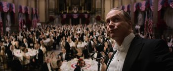 Movie still from “Fantastic Beasts and Where to Find Them” (2016), directed by David Yates – A man standing in front of a crowd of people in formal wear; Medium shot, Low angle