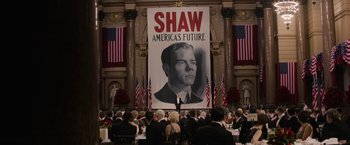 A man standing in front of an audience under a large poster