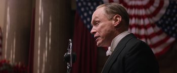 Movie still from “Fantastic Beasts and Where to Find Them” (2016), directed by David Yates – A man in a suit is speaking into a microphone; Close Up shot, Low angle