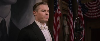 Movie still from “Fantastic Beasts and Where to Find Them” (2016), directed by David Yates – A man in a tuxedo standing in front of american flags; Close Up shot, Low angle