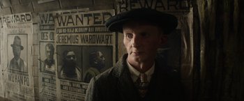 Movie still from “Fantastic Beasts and Where to Find Them” (2016), directed by David Yates – A man in a hat and a suit standing in front of a poster; Close Up shot, Over the shoulder angle