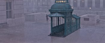 Movie still from “Fantastic Beasts and Where to Find Them” (2016), directed by David Yates – A person walking in the rain next to a subway station; Extreme Wide shot, High angle