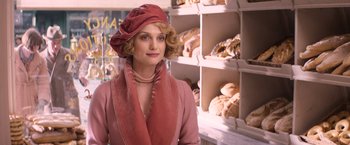 Movie still from “Fantastic Beasts and Where to Find Them” (2016), directed by David Yates – A woman wearing a pink hat and a pink dress in front of shelves of baked goods; Medium shot, Over the shoulder angle