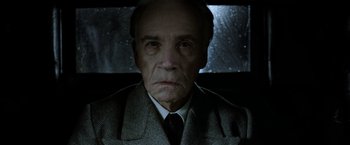 Movie still from “Fantastic Beasts: The Crimes of Grindelwald” (2018), directed by David Yates – An older man in a suit and tie looking at the camera; Close Up shot, Low angle
