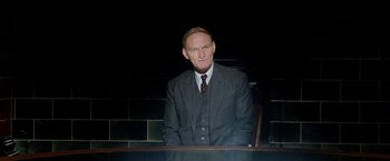 Movie still from “Fantastic Beasts: The Crimes of Grindelwald” (2018), directed by David Yates – A man in a suit and tie sitting at a table; Medium shot, Low angle