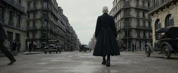 Movie still from “Fantastic Beasts: The Crimes of Grindelwald” (2018), directed by David Yates – An older man in a long coat walking down a street; Wide shot, Low angle