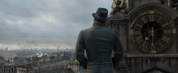 Movie still from “Fantastic Beasts: The Crimes of Grindelwald” (2018), directed by David Yates – A man standing on the side of a building looking out over a city; Medium shot, Over the shoulder angle