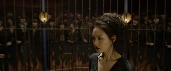 Movie still from “Fantastic Beasts: The Crimes of Grindelwald” (2018), directed by David Yates – A woman standing in front of a crowd of people behind a fence; Close Up shot, Over the shoulder angle