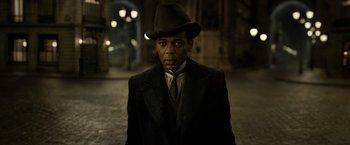 Movie still from “Fantastic Beasts: The Crimes of Grindelwald” (2018), directed by David Yates – A man wearing a suit and a hat in the dark; Close Up shot, Over the shoulder angle