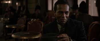 Movie still from “Fantastic Beasts: The Crimes of Grindelwald” (2018), directed by David Yates – A man sitting in front of a chair in a room; Close Up shot, Over the shoulder angle