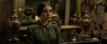 Movie still from “Fantastic Beasts: The Crimes of Grindelwald” (2018), directed by David Yates – A beautiful woman in a green dress sitting in front of a clock; Close Up shot, Over the shoulder angle