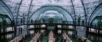Movie still from “Fantastic Beasts: The Crimes of Grindelwald” (2018), directed by David Yates – People are standing around a long table in a large room; Extreme Wide shot, High angle