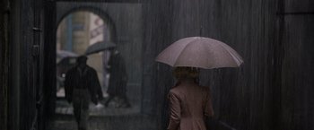 Movie still from “Fantastic Beasts: The Crimes of Grindelwald” (2018), directed by David Yates – A woman holding an umbrella while standing in the rain; Wide shot, High angle