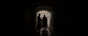 Movie still from “Fantastic Beasts: The Crimes of Grindelwald” (2018), directed by David Yates – Two people are standing in a dark tunnel; Wide shot, Over the shoulder angle
