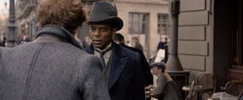 Movie still from “Fantastic Beasts: The Crimes of Grindelwald” (2018), directed by David Yates – A man wearing a hat and a suit; Close Up shot, Over the shoulder angle